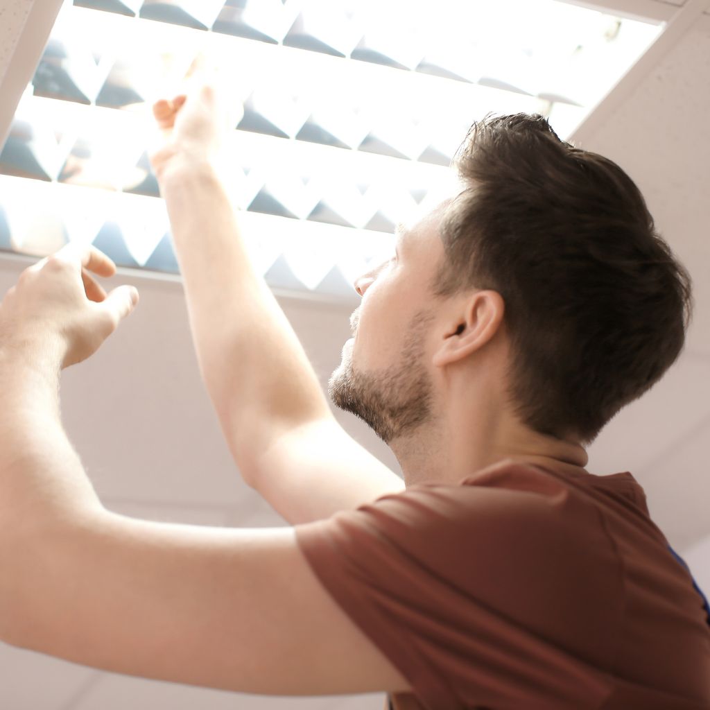 Young adult man replacing fluorescent lightbulb in office. Electrical Handyman Services in Fredericksburg VA Prime Baths LLC